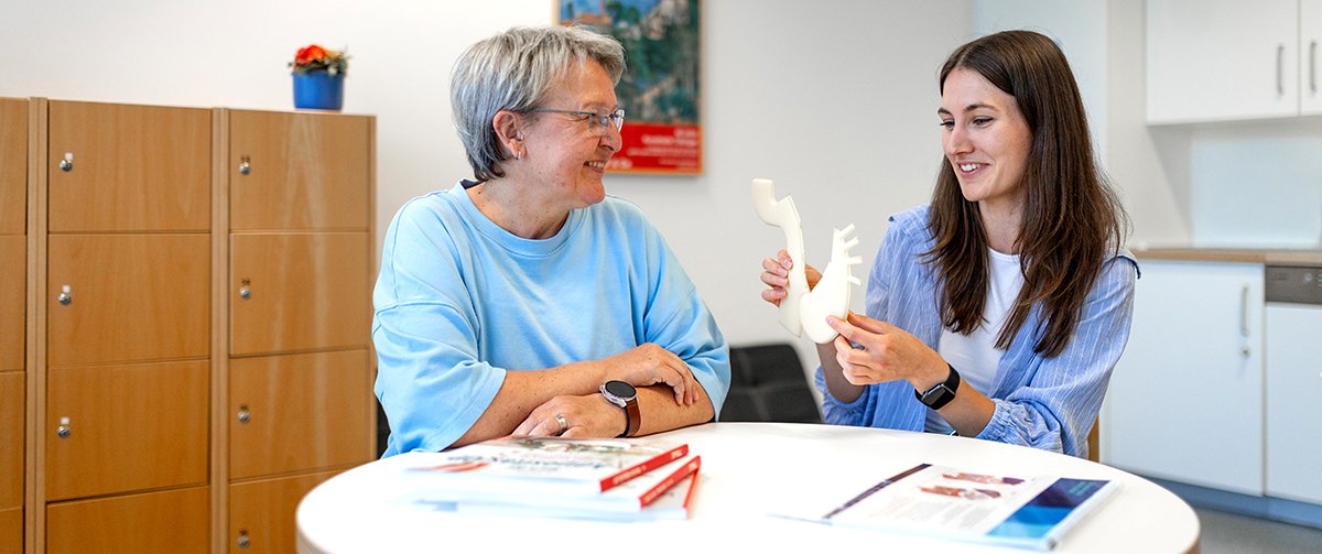 Die Ernährungswissenschaftlerin Jasmin Ketel sitzt mit der Patientin Kerstin Schäfer an einem Tisch und zeigt ihr ein Modell des Magen-Bypass.